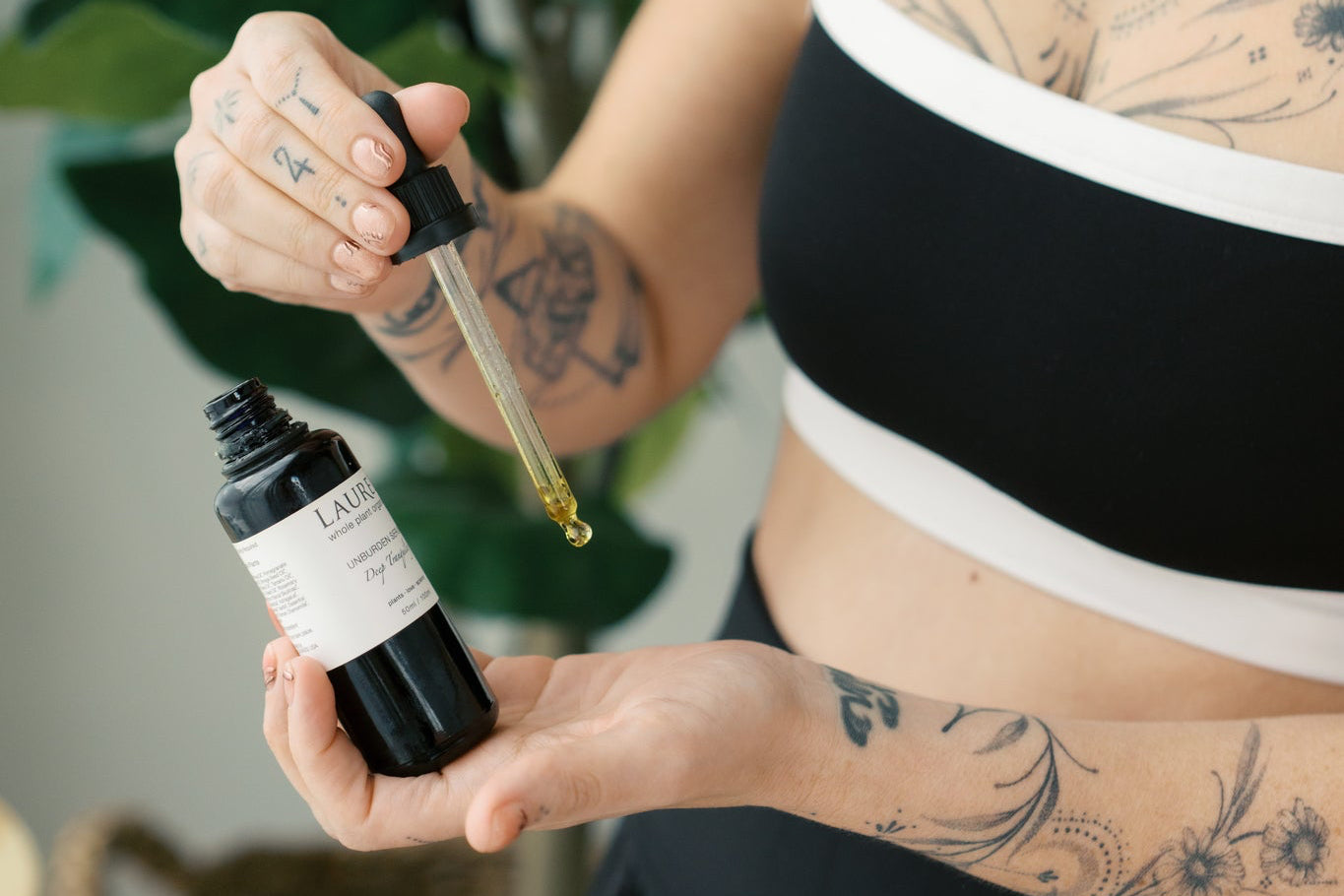 Woman holding a dropper with a black bottle, surrounded by greenery